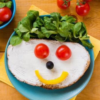 Um prato colorido com frutas, verduras e pão em forma de rosttinho feliz.
