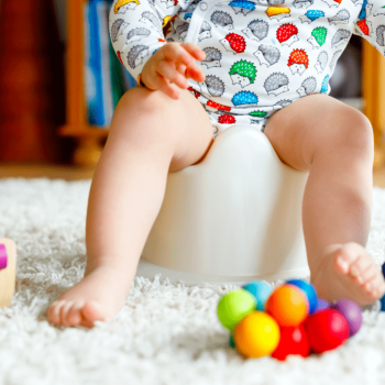 Criança sentada em um penico para fazer cocô, cercada de brinquedos coloridos.