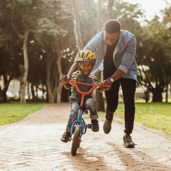 Como criar boas lembranças de infância para seus filhos? Para criar boas lembranças, pai ensina filho a andar de bicicleta em um parque.