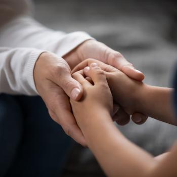 a imagem mostra as mãos de uma mulher adulta segurando as mãos de uma criança