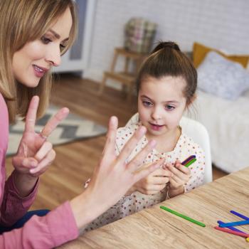 Uma mulher mostra números com os dedos, prática comum no ensino de matemática para crianças, para uma menina que a observa. 