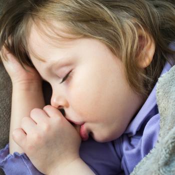 Criança dormindo com uma das mãos no cabelo enquanto chupa o dedo. 