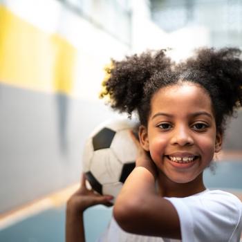 Criança praticando esportes em uma quadra, segurando uma bola de futebol