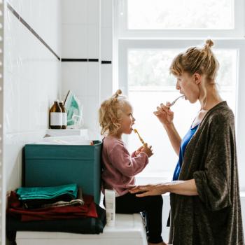 Mãe escova os dentes com a filha, ensinando a importância da higiene bucal para crianças.