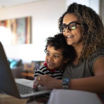 Mãe empreendedora mexe no computador com o filho no colo.