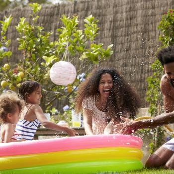 Foto de uma família se divertindo em um ambiente aberto com uma piscina de plástico colorida