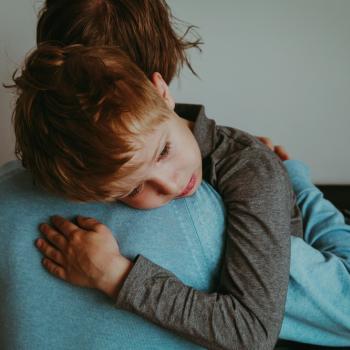 Um menino com olhar triste recebe o abraço de seu pai.