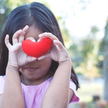 Menina segurando um coração vermelho em frente ao rosto 