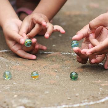 Brincadeiras indígenas para aprender e se divertir com as crianças Duas crianças brincam de bola de gude no chão em um círculo desenhado de giz. A foto faz alusão ao tema de brincadeiras indígenas.