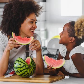 Foto de mãe e filha fazendo um lanche com frutas da estação, nesse caso melancia