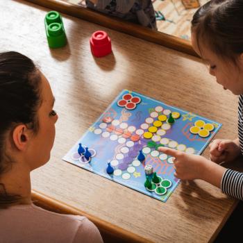 Uma mulher que aparenta ser mãe da criança que está ao lado, as duas estão jogando um jogo de tabuleiro em casa.