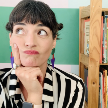 Monteiro Lobato - ler ou não ler para as crianças? Flávia Scherner com expressão pensativa olhando para cima, ao fundo parede pintada na cor verde e estante com livros coloridos.