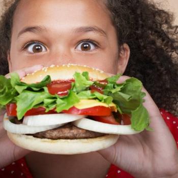 Menina segurando um hamburguer caseiro com bastante salada de vegetais e cebola