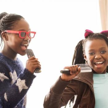 Duas meninas cantam usando o microfone, uma das formas de aprender brincando.
