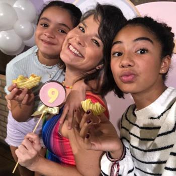 Samara Felippo e suas duas filhas em ambiente de festa de aniversário, segurando docinhos nas mãos e sorrindo para a fotografia.