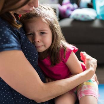 criança no colo de uma mulher adulta, sendo confortada pois está chorando.