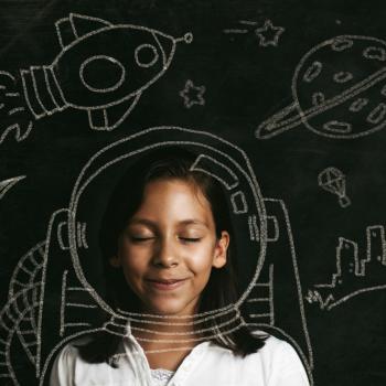 Criança com sorriso no rosto em meio a desenhos feitos no quadro escolar e também um capacete espacial desenhado sobre a imagem da criança.
