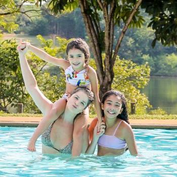  Samara Felippo na piscina com suas duas filhas, todas sorrindo em um dia de sol.