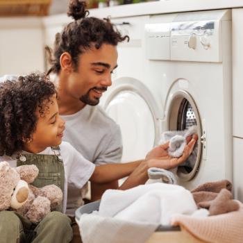 Homem e criança colocando roupas na máquina de lavar.