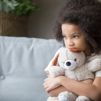 Imagem de uma criança sozinha segurando um bicho de pelúcia, olhando de forma distraída para o nada, este olhar pode ser um sintoma de síndrome de asperger