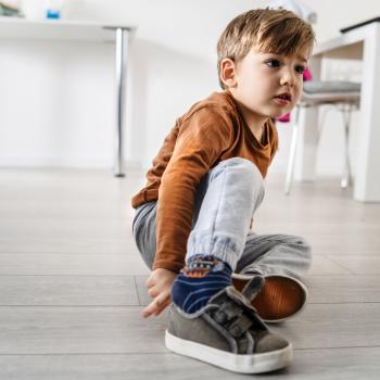 garotinho sentado no chão da sala de casa calçando tênis sozinho