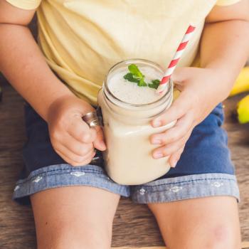 3 receitas de vitaminas de frutas e seus benefícios para as crianças criança sentada ao redor de algumas bananas, segurando vitamina