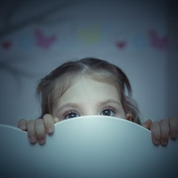 criança se esconde atrás de cabeceira de cama em quarto infantil, rosto com expressão assustada.