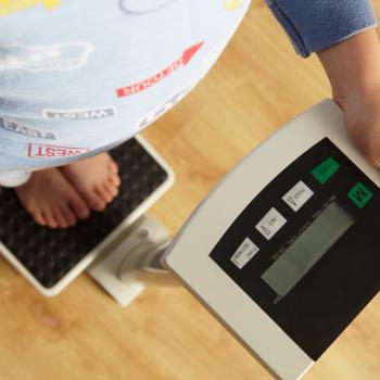 a imagem representa a obesidade infantil mostrando uma criança conferindo o seu peso em uma balança