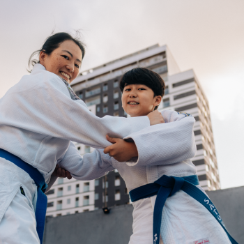 Mãe e filho vestindo kimono com uma faixa azul fingindo estarem lutando enquanto olham para a câmera 