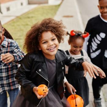 Foto de 4 crianças sorrindo, fantasiadas e carregando uma cesta de abóbora para a festa de halloween.