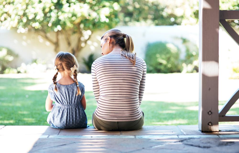 A relação com crianças agressivas é aqui representada pela imagem de uma mãe e uma filha sentadas de costas para foto. A mãe está falando algo para a criança. 