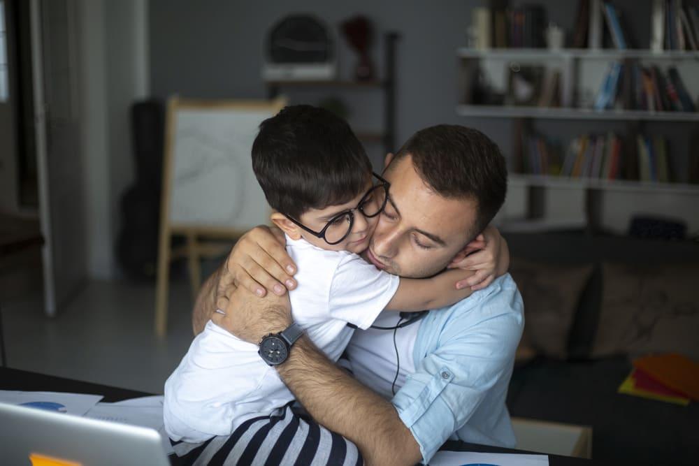 Pai e filho se abraçam dentro de uma sala