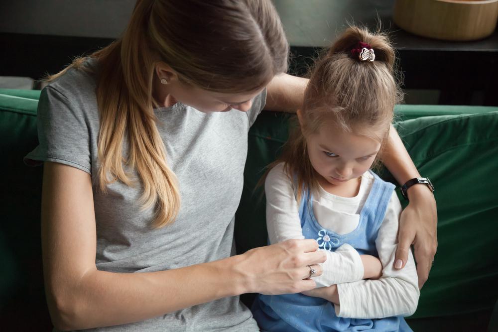 Sentadas em um sofá verde, a mãe tenta dialogar com a filha que está emburrada de braços cruzados.