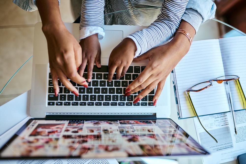 A foto mostra as mãos de uma mulher adulta e de uma criança digitando em um notebook para encontrar as respostas das perguntas difíceis feitas pela criança