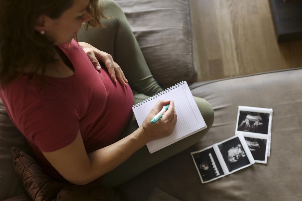 Mulher grávida faz uma lista em caderno com nomes de criança para seu bebê