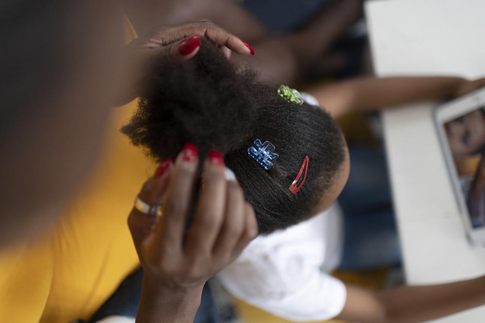 Uma mãe faz um coque no cabelo da filha, com presilhas