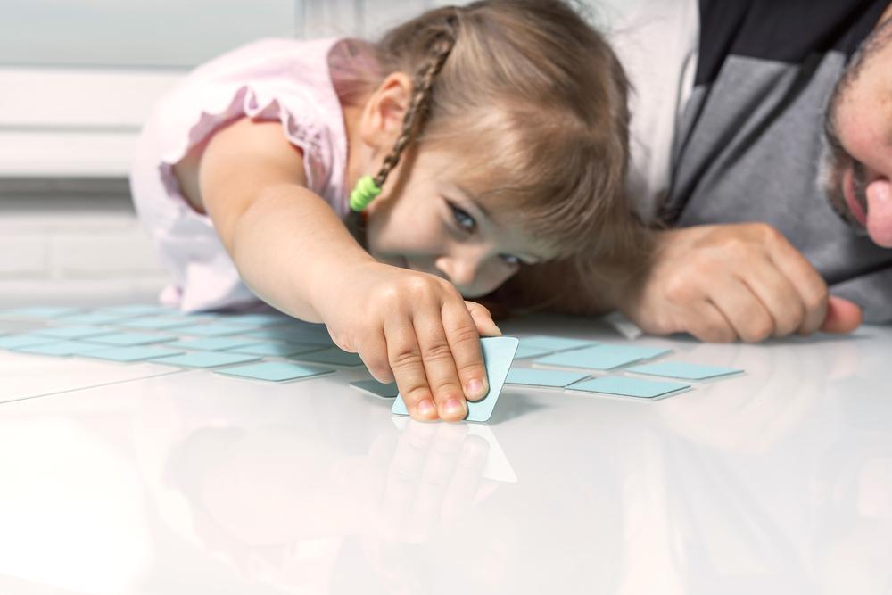 Uma menina e um adulto brincam de jogo de memória, um dos tipos de jogos educativos.