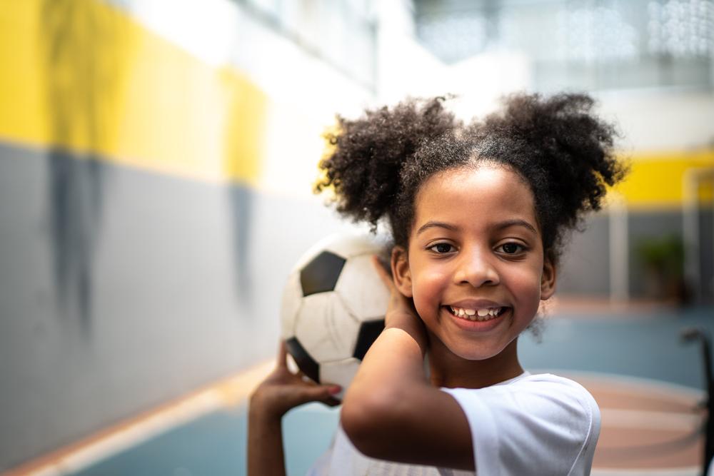 Criança praticando esportes em uma quadra, segurando uma bola de futebol