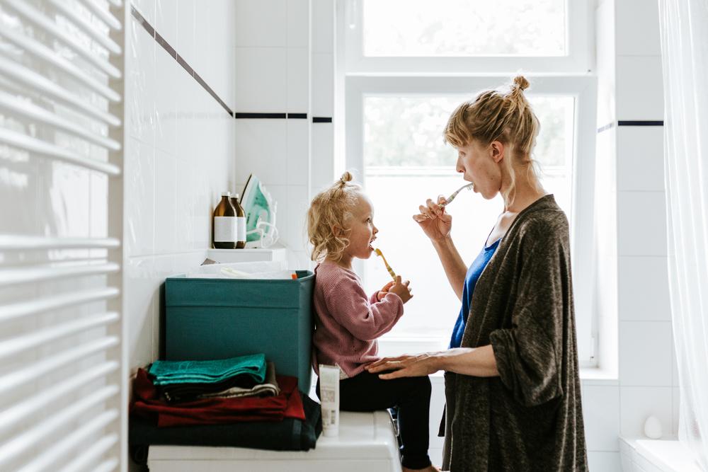 Mãe escova os dentes com a filha, ensinando a importância da higiene bucal para crianças.