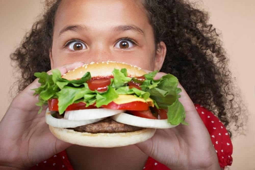 Menina segurando um hamburguer caseiro com bastante salada de vegetais e cebola