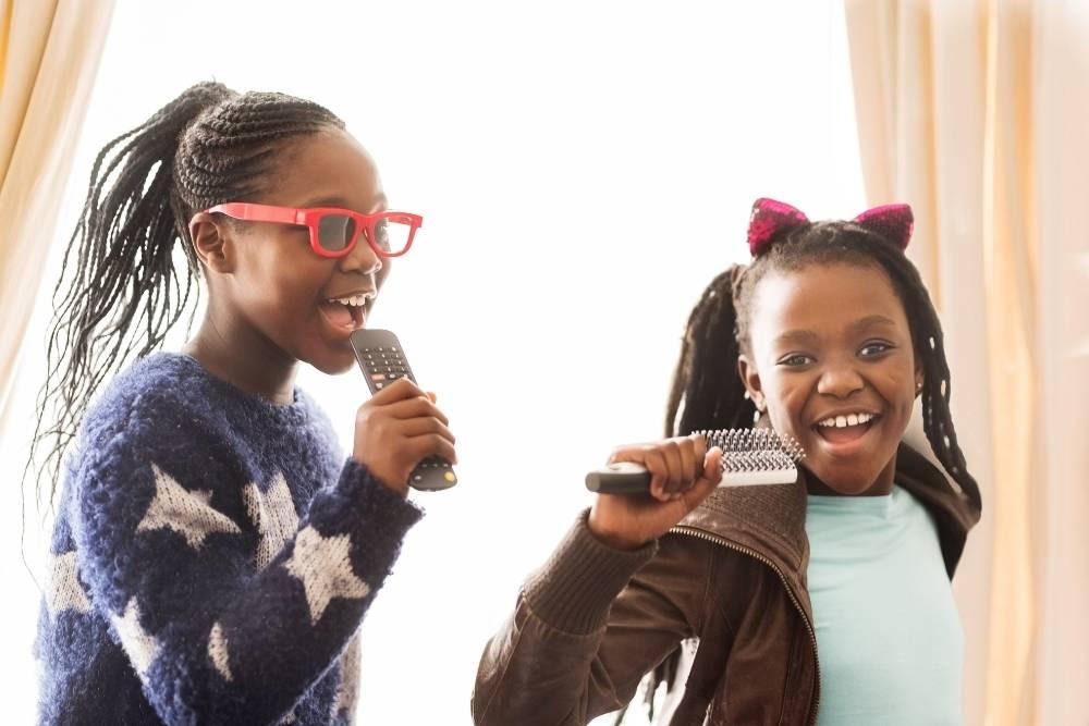 Duas meninas cantam usando o microfone, uma das formas de aprender brincando.