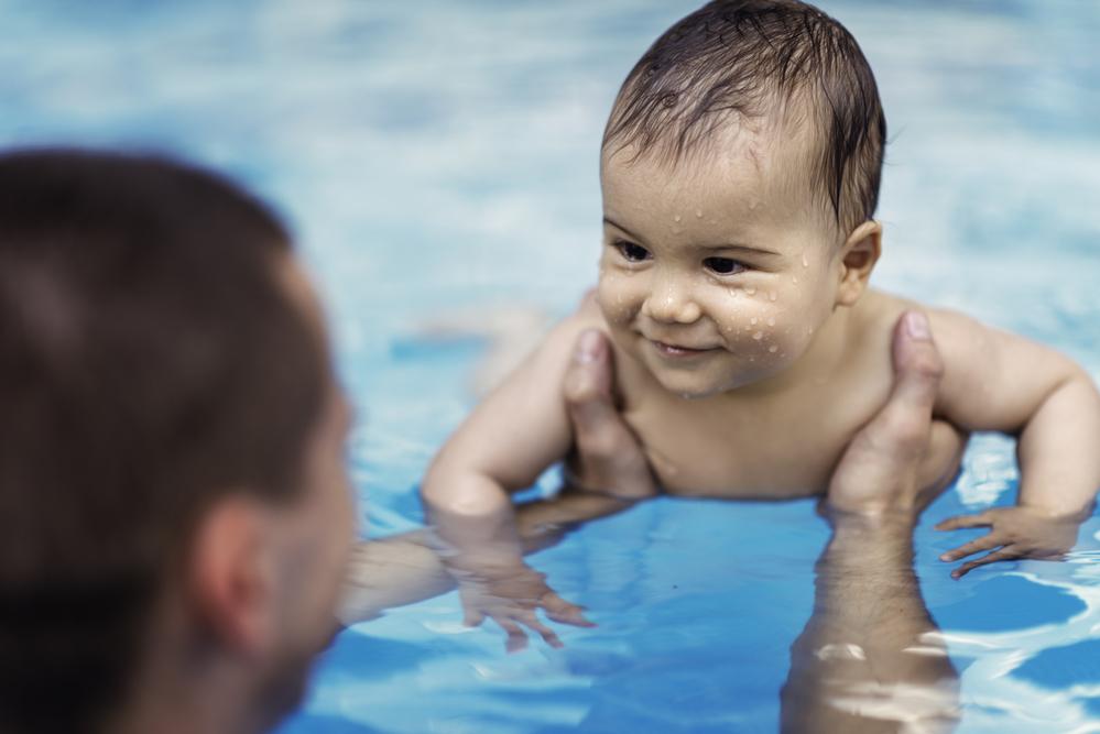 Homem segurando bebê sorridente na piscina.