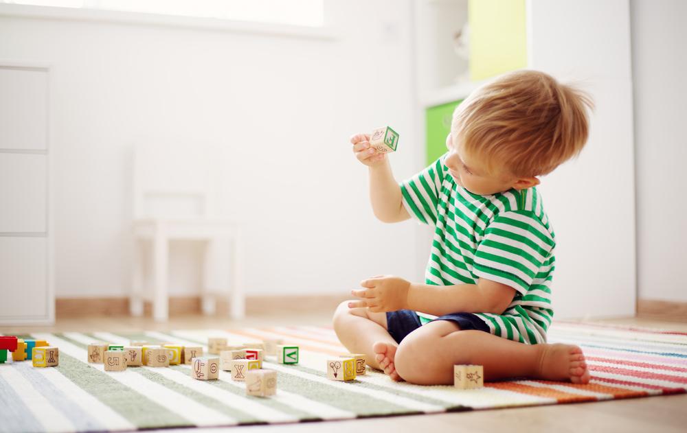 Criança sentada brincando sozinha com dadinhos no tapete da salinha de brinquedos.