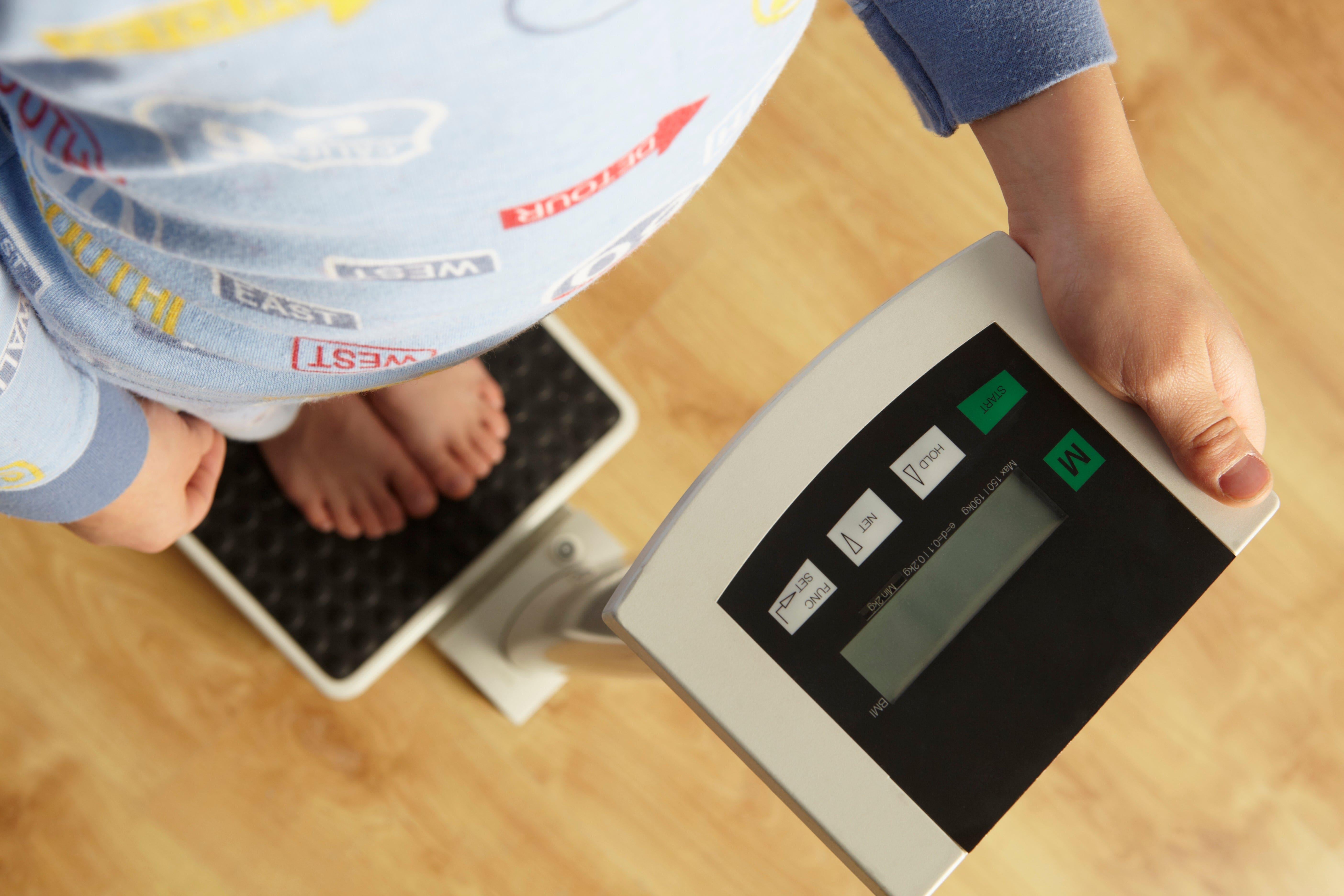 a imagem representa a obesidade infantil mostrando uma criança conferindo o seu peso em uma balança