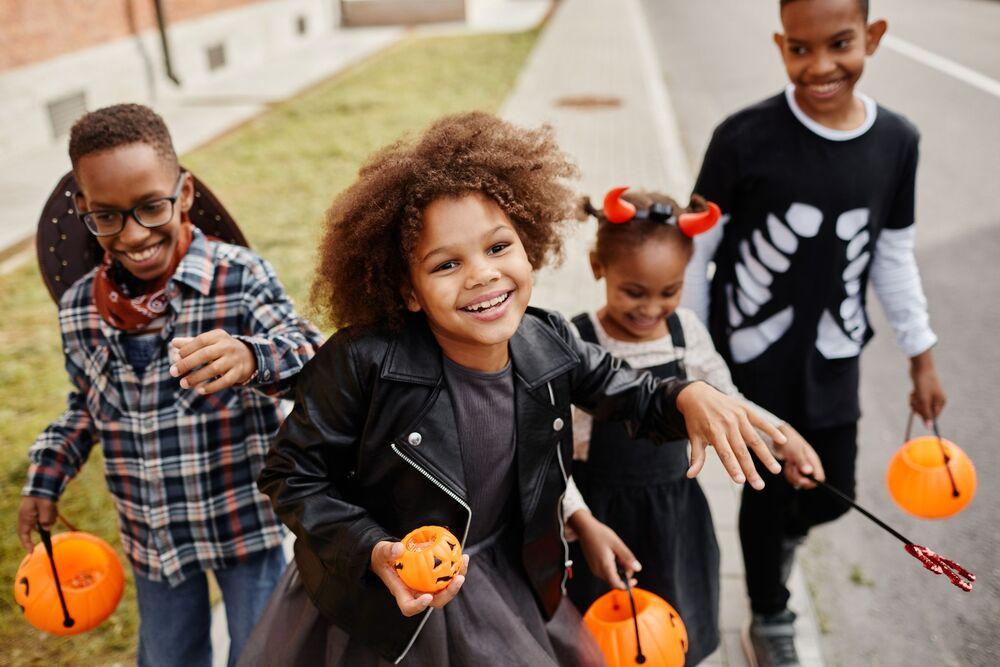 Foto de 4 crianças sorrindo, fantasiadas e carregando uma cesta de abóbora para a festa de halloween.